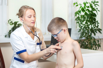 Lekarka pediatra w białym kitlu bada stetoskopem chłopca w niebieskich okularach. - obrazy, fototapety, plakaty