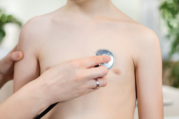 Dłoń lekarki trzyma głowicę stetoskopu przystawioną do piersi dziecka podczas badania.  - obrazy, fototapety, plakaty