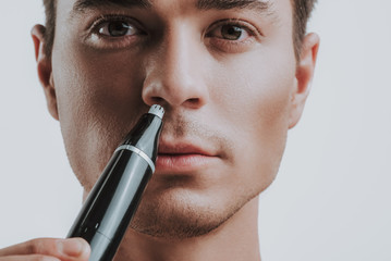 Close up of calm man using modern nose trimmer