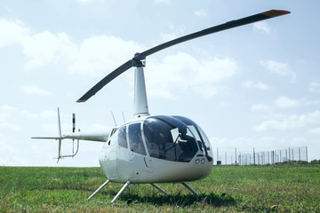 Small light helicopter parked on grass airport. Most popular light helicopters with twin blades and a single engine