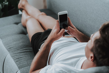 Man in underwear lying on sofa and using his smartphone - obrazy, fototapety, plakaty