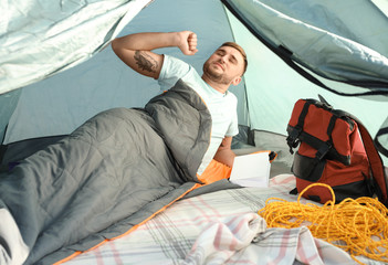 Young man stretching in sleeping bag inside of camping tent