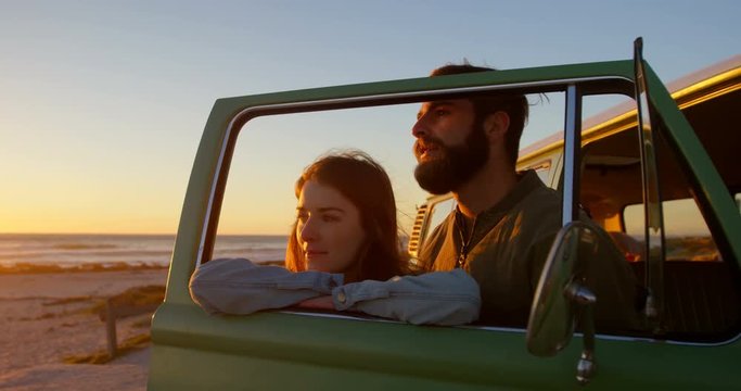 Young couple standing by van window during sunset on beach 4k