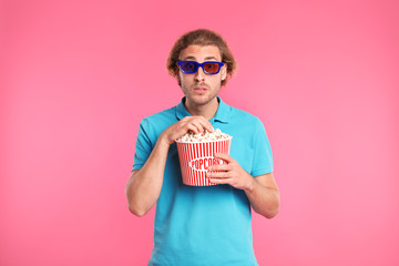 Naklejka premium Emotional man with 3D glasses and popcorn during cinema show on color background