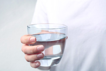 Woman holding glass with fresh water against light background, closeup