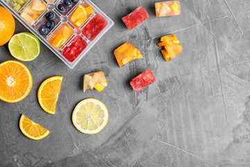 Flat lay composition with ice cube tray and fresh fruits on grey background. Space for text