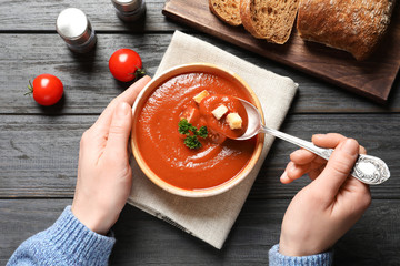 Woman eating fresh homemade tomato soup at wooden table, top view