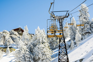 Mount Baldy (Mt San Antonio) ski lift on a sunny day; snow covering the ground and the pine trees,...