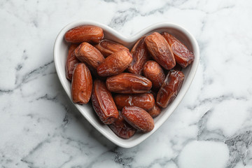 Heart shaped bowl with sweet dried date fruits on marble background, top view
