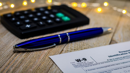 Tax still life business finance concept, form W9, with calculator, pen shallow DOF