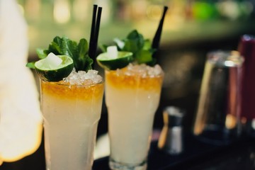 Mojito classic cocktails on bar. Close-up cold cocktail with crushed ice, mint and slice of lime with burning sugar cube on glass at dark background. Shaker and jigger barmen equipment.