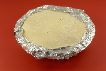 Frozen apple pie prepared for baking with aluminum over edge of crust and slits in top for more...