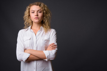 Young beautiful businesswoman with curly blond hair against gray