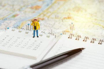 Travel planning or year plan for vacation or start new journey concept, miniature people traveller, backpacker man standing on calendar with pen and city map