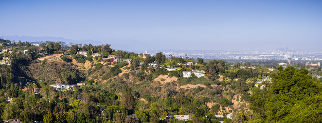Fototapeta premium Scattered mansions on one of the hills of Bel Air neighborhood; the downtown skyscrapers visible in the background through a hazy atmosphere; Los Angeles, California