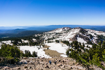 Fototapeta na wymiar Hiking views from the trail to Lassen Peak with ridges and valleys still covered in snow and Lake Almanor visible in the background; Lassen Volcanic National Park, Shasta County, Northern California