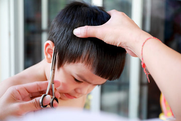 Naklejka premium change the face : little asian boy is getting haircut by hairdresser