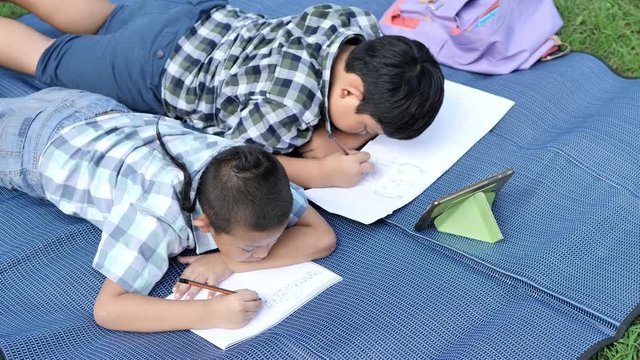Two Asian boys drawing on mat in a book at park...concept education