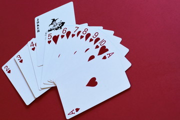 Imagination, allegory. Joker as original decision, driving force. Fan of playing cards of suit of hearts and black joker on red background.