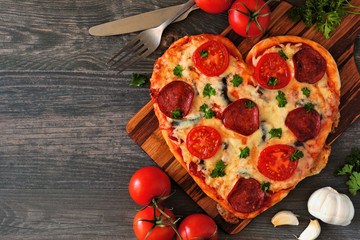 Heart shaped pizza for Valentines Day over a dark wood background. Top view, side orientation....