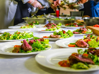 Cooked Roast Beef, Fresh Salad And Tomatoes Served On White Plates. Cooking Master Class, Workshop with People Learning How to Cook Around the Table.