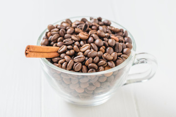 Glass bowl with coffee beans and cinnamon stick on white rustic table.