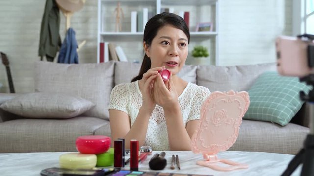 Young Asian cute artist woman beauty vlogger doing cosmetic makeup tutorial vlog showing products looking cellphone. blogger recording viral clip to share on social media live streaming for Internet