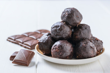 Chocolate-drenched balls of grated nuts and dried fruits in a bowl on a white wooden table.