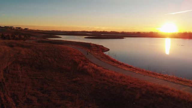 Electric Skateboarding on Curvy Path with Lake and Sun at Sunrise Aerial Stationary View