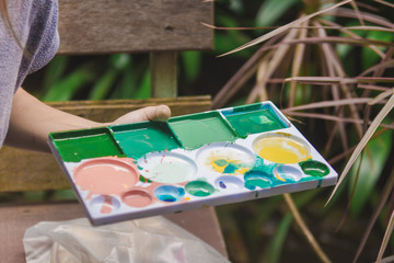 Woman holding palette of color paints with natural tree background.