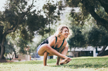 smiling caucasian woman performing yoga shoulder pressing pose while exercising on green lawn
