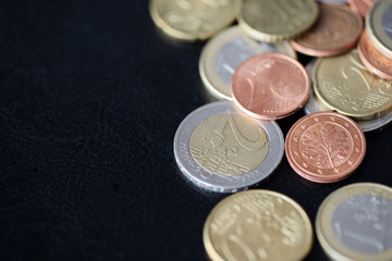 A pile of euro coins scattered on a dark surface close up