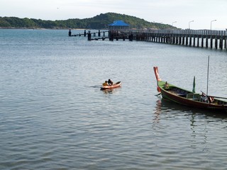 Fishing boat with fishers. Old long pier. Two people in a canoe on the surface of the water sort the catch in the evening at the end of the day. Traditional Asian Longtail Boat and fishermen in a sea