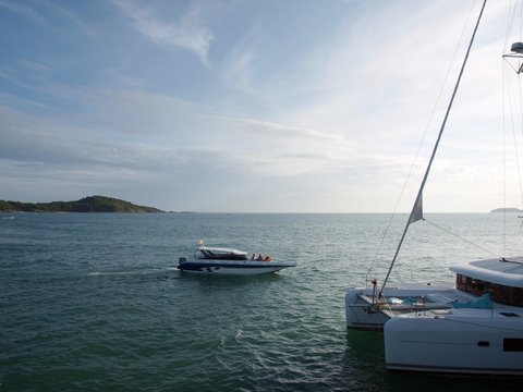 Boat and yacht on the sea. The part of sailing yacht in foreground, speedboat on the surface of water on the center of  the image, islands on the horizon on the background of picture