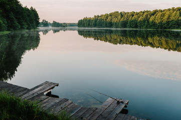 Fishing rod, spinning reel on the background pier river bank. Sunrise. Fog against the backdrop of...