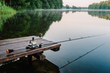 Fishing rod, spinning reel on the background pier river bank. Sunrise. Fog against the backdrop of lake. Misty morning. wild nature. The concept of rural getaway. Article about fishing day.