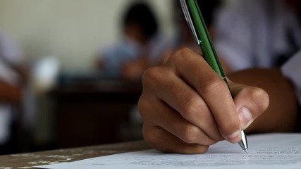Student holding pen and writing final exam in examination room or study in classroom.