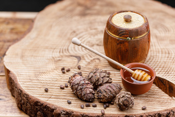 Barrel with honey and a spoon on a large wooden sawn and pine nuts and cones. Textured wood products.