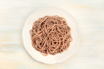 A plate of soba, buckwheat noodles, shot from above on a pale wooden background with a place for text