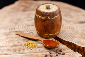 A wooden spoon with honey and a keg on a textured wooden saw.
