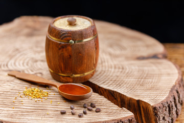 A wooden spoon with honey and pollen and a barrel on a textured wooden saw.