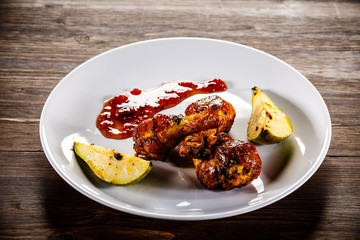 Grilled chicken drumsticks with pear on wooden background