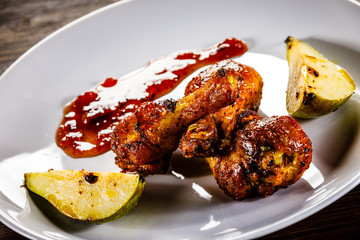 Grilled chicken drumsticks with pear on wooden background