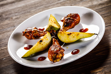 Grilled chicken drumsticks with pear on wooden background