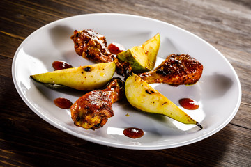 Grilled chicken drumsticks with pear on wooden background