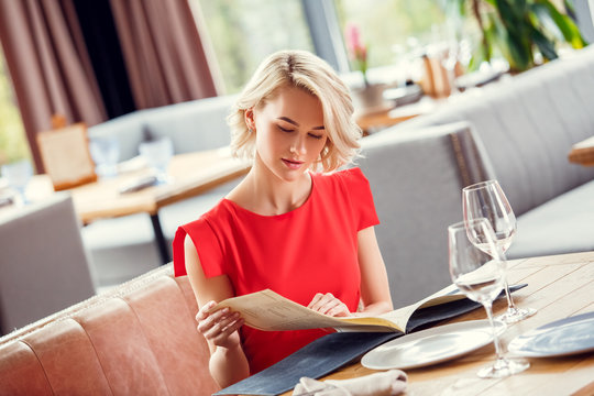 Young woman dining in restaurant sitting looking at wine list curious