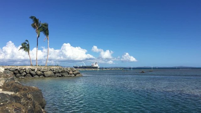 Small waves on a shallow water over the reef formed from the light breeze on a bright sunny day with a blue sky and tanker anchored in the background in Fiji
