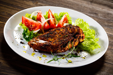 Grilled chicken fillet and vegetables on wooden background