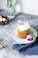 Easter cake kulich. Traditional Easter sweet bread decorated meringue and pink roses on plate on gray stone table background. Copy space.