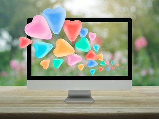 Colorful love heart balloon with desktop modern computer on wooden table over blur flower and tree in park, Business internet dating online, Valentines day concept
